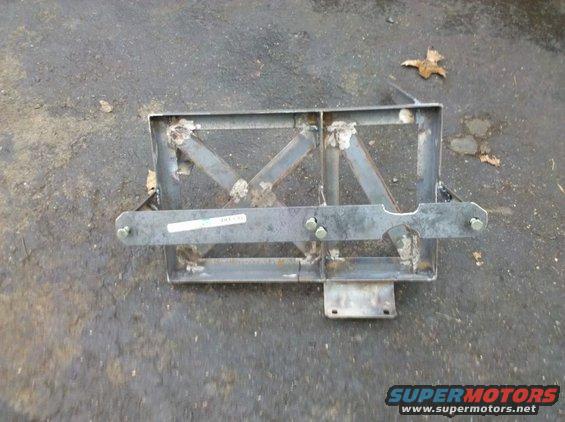 metal bracket with bolts and a sticker on it, sitting on asphalt