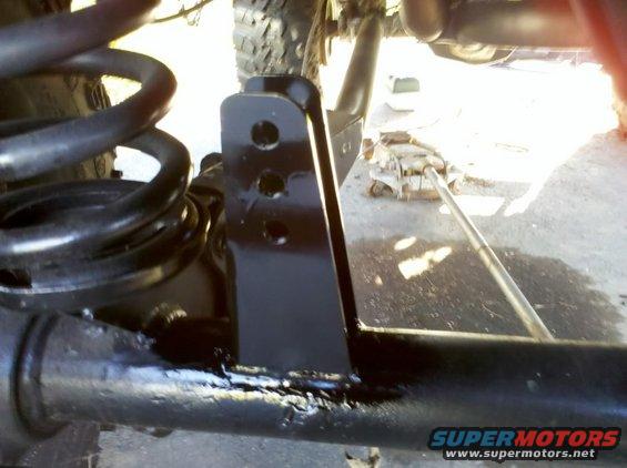 Close-up of black suspension parts and a coil spring, with a jack visible in the background