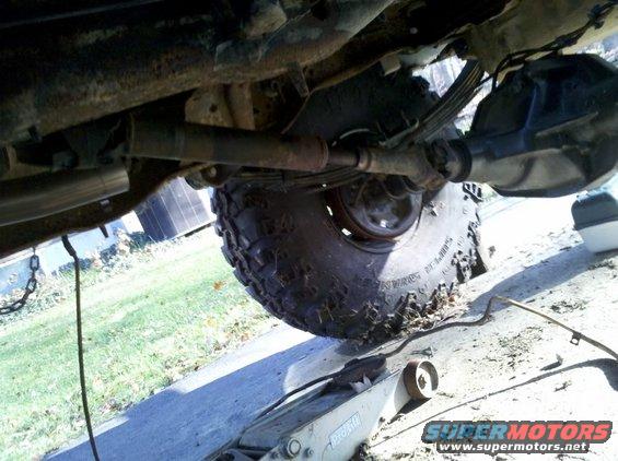 Undercarriage of a vehicle with a large tire, leaf springs, and a differential visible, supported by a floor jack