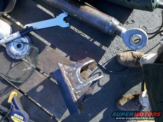Welding project with metal parts, wrench, marker, grinder disc, and clamp on wooden surface