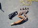 1989 Ford Bronco - Two exhaust manifolds, a gasket, and bolts are laid out on an asphalt surface, likely for a vehicle repair or upgrade.