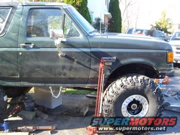 Green Ford Bronco on jacks, looks like it's being worked on. Big off-road tires