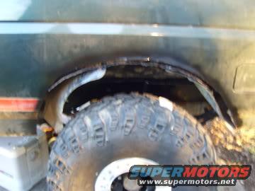 Close-up of a vehicle's rear wheel well, showing the tire and fender area. Some rust is visible