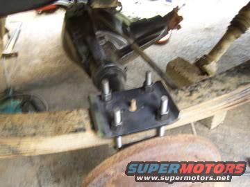 Rear axle assembly with U-bolts and leaf spring mount. Rusty drum brake visible