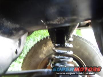 Close-up of a vehicle's suspension spring and tire, with SuperMotors.net logo visible