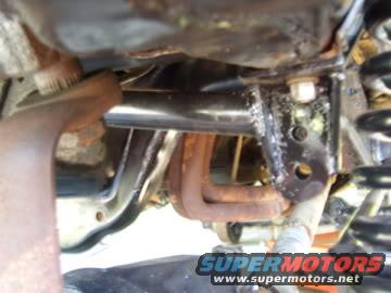 Underside of a vehicle showing exhaust manifold and suspension components. Supermotors.net logo visible