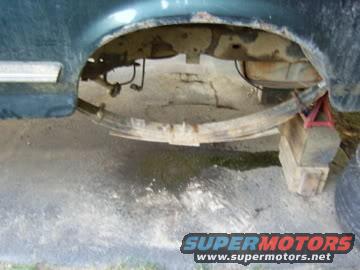 Rear wheel well area of a vehicle, showing leaf spring, gas tank, and suspension components. Vehicle is on jack stands