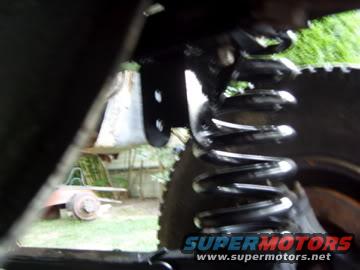 Close-up of a coil spring and tire tread, with a SuperMotors logo at the bottom right