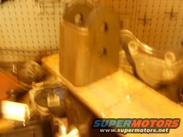 Metal bracket with two holes on a wooden surface, blurry background