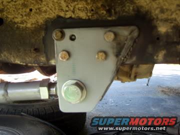 Close-up of a gray metal suspension bracket bolted to a vehicle frame, with part of a tire visible