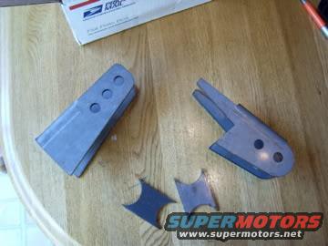Two metal brackets and two small metal pieces on a wooden surface