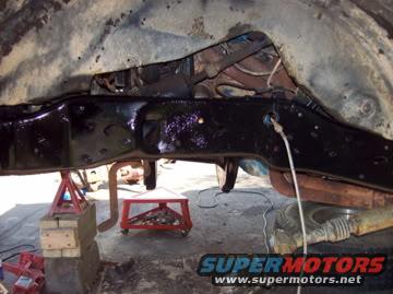 Vehicle frame and suspension parts on jack stands, showing rust and black undercoating