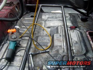 Interior view of vehicle with roll cage installation, angle grinder, and tools
