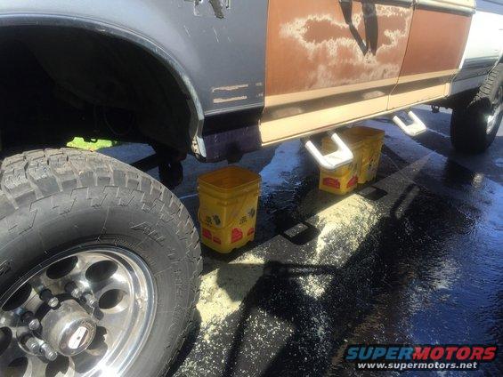 Side view of a truck with a large tire in the foreground. Yellow buckets are placed under the frame