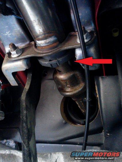 Close-up of a vehicle's steering column linkage with a red arrow pointing to a gray plastic clip