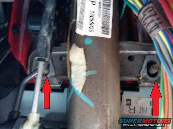 Close-up of steering column with red arrows pointing to mounting brackets and wiring harness