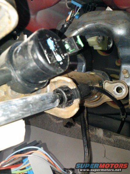 Close-up of black steering column components with visible wiring and a metal rod. Red paint is visible in the upper left