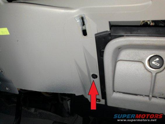 Close-up of a gray plastic panel with a screw and a red arrow pointing to it, next to a closed compartment with an ashtray symbol