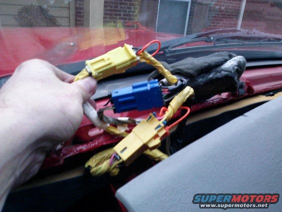 Hand holding yellow airbag connector near dashboard wiring in a 1998 Chevrolet C/K Pickup