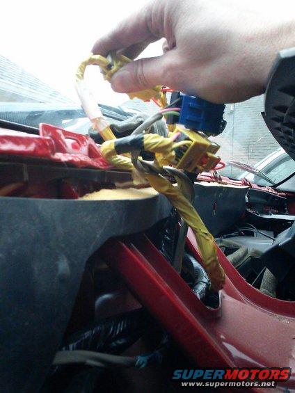 Hand connecting yellow wiring harness connectors under red dashboard panel