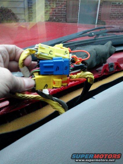 Hand holding yellow and blue wiring harness connectors with labels A, C, and D. Red dashboard visible