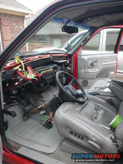 Red pickup truck interior with disassembled dashboard, gray leather seats, and tools on the floor