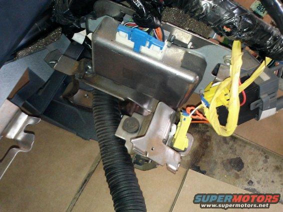 Airbag control module with blue and yellow connectors, attached to metal bracket and black corrugated tubing