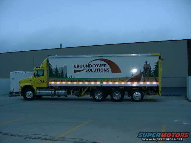 Side view of a yellow semi-truck with a white trailer displaying "GROUNDCOVER SOLUTIONS" logo
