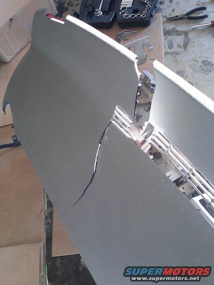 Cracked dashboard panel with chrome trim visible underneath. Tools are on a table in the background