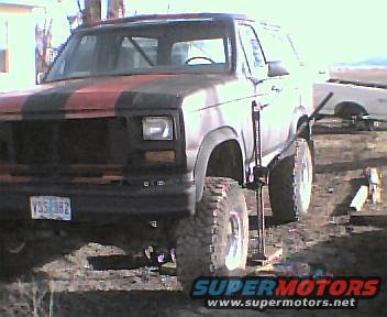 1983 Ford Bronco with red and black racing stripes, jacked up on the front passenger side