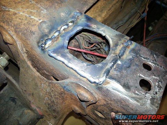 Close-up of a rusty metal frame section with fresh welds and a bundle of wires visible through a hole
