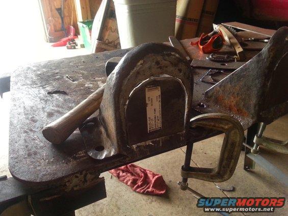 metal bracket clamped to workbench with a hammer nearby. Label is visible on the bracket