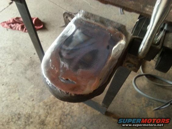 Metal part with visible welds and grinding marks, held by clamps