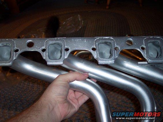 Hand holding a silver exhaust manifold with four ports visible