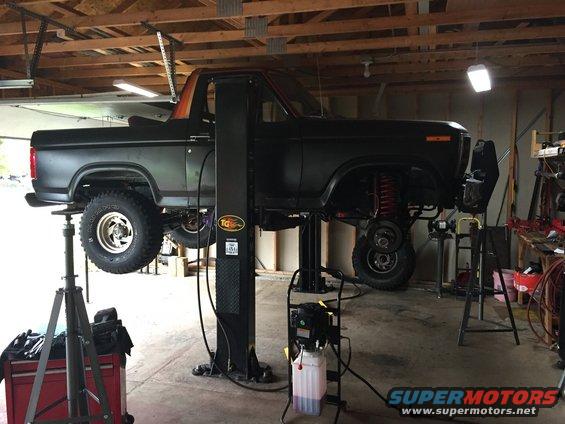 Dark-colored Ford Bronco on a lift, viewed from the side