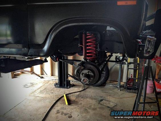 Front suspension and brake assembly of a vehicle on a lift, showing red coil springs and brake rotors
