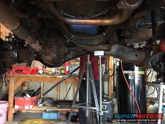 Underside of a vehicle with a differential, exhaust, and suspension parts supported by a jack