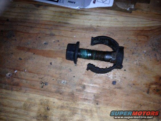 Bolt with a broken rubber bracket on a wooden surface. Text on a box in the background reads 'MWV'