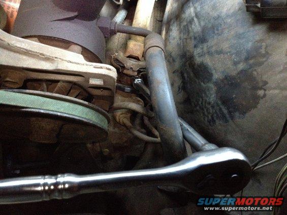 Ratchet wrench working on engine components, near a belt and pulley