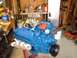1978 Ford F-250 - Blue V8 engine on a stand in a workshop setting with tools and equipment in the background.