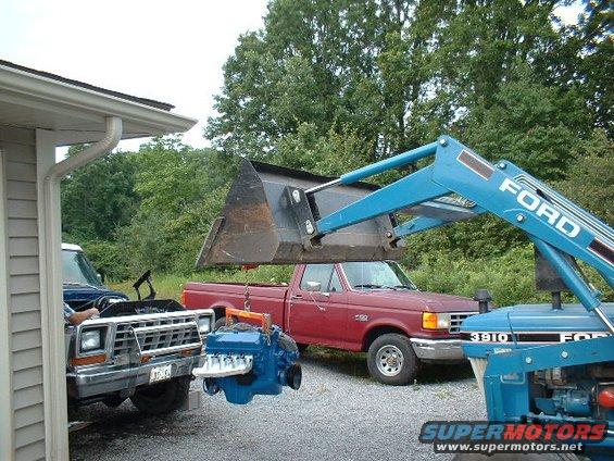 Red Ford pickup truck with engine being lowered by loader; front of another Ford truck visible