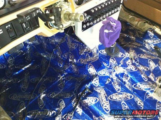 Car interior with sound deadening material on the floor and dashboard components exposed