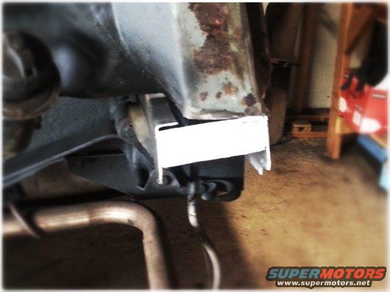 Close-up of rusty vehicle frame with a white metal bracket and exhaust pipe