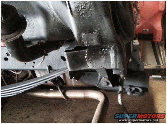 Close-up of vehicle frame, leaf spring, and exhaust pipe. Some rust and wear visible