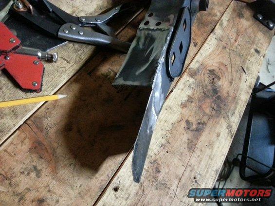 Welding clamp and pencil on a wooden workbench next to a metal part being worked on
