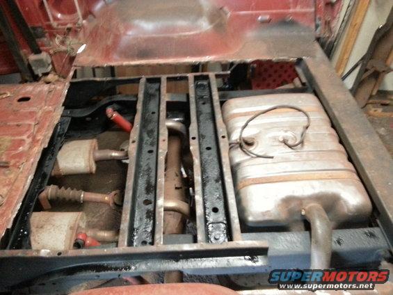 Underbody of a vehicle with exhaust system and fuel tank visible. Some rust and repair work apparent