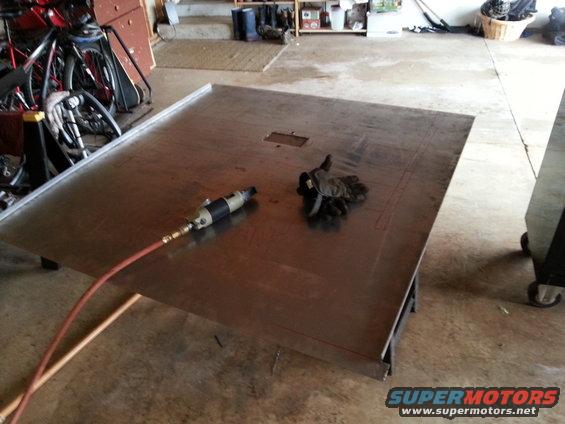 Large metal sheet on sawhorses with an air-powered tool and gloves on top