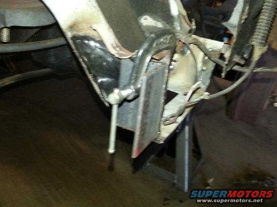 Vehicle front end, possibly a truck or SUV, on jack stands. Chrome bumper and grille area visible