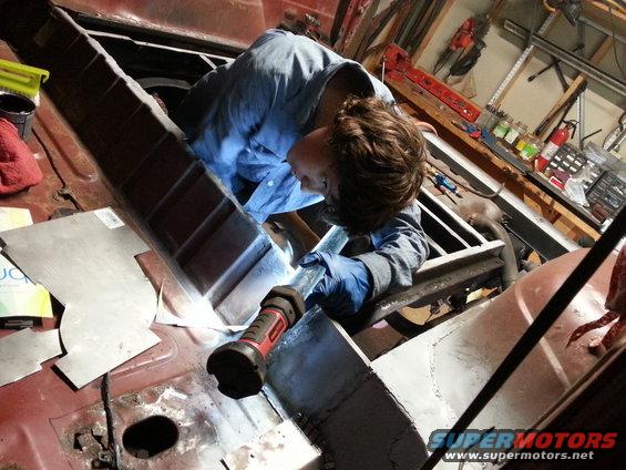 Person welding inside a red vehicle's interior, with sheet metal and tools visible