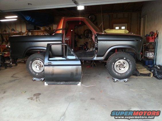 Gray and orange Ford Bronco with driver's door off, raised on jack stands in a garage